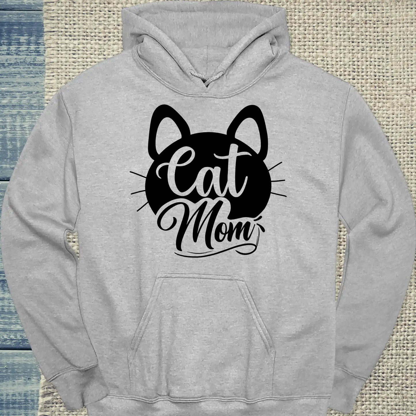 Mach es dir gemütlich mit dem Cat Mom schnurr - Hoodie, einem grauen Kapuzenpullover aus weicher Baumwolle mit schwarzem Katzen-Gesicht und "Cat Mom" Schriftzug in eleganter Schreibschrift auf der Vorderseite.